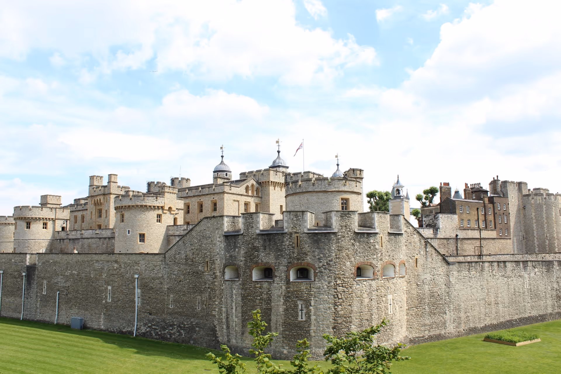 Stone castle with battlements and towers under a partly cloudy blue sky, surrounded by green grass.