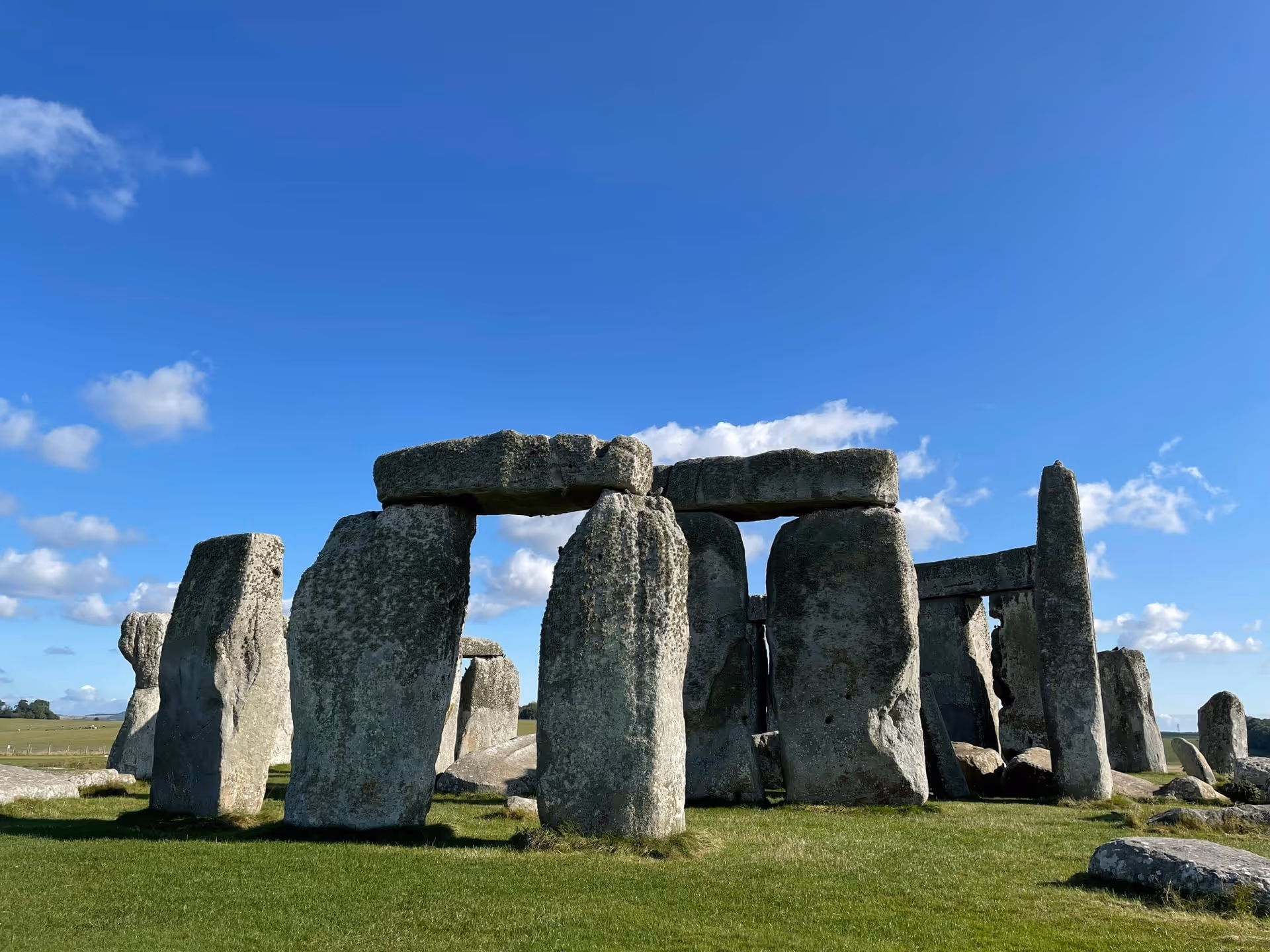 Stonehenge prehistoric stone monument under a clear blue sky with scattered clouds.